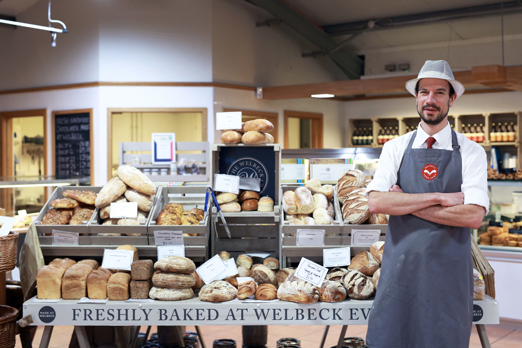 Team member standing beside artisan bakery display at Welbeck Farm Shop and Harley Café