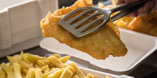 Freshly battered fish being lifted with a spatula above golden chips at The Fishermen’s Chippy