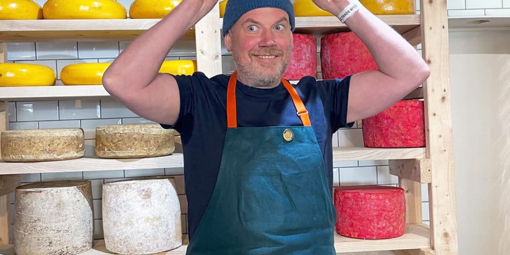 Cheesemonger holding a large wheel of artisan Irish cheese at Indie Füde in Belfast.