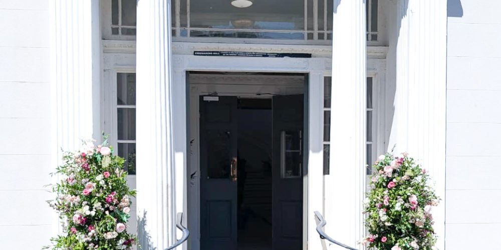 Entrance of Woodbourne House wedding venue with white columns and floral displays.