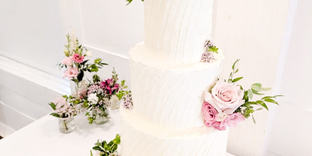 Three-tier white wedding cake with blush pink flowers at Woodbourne House.