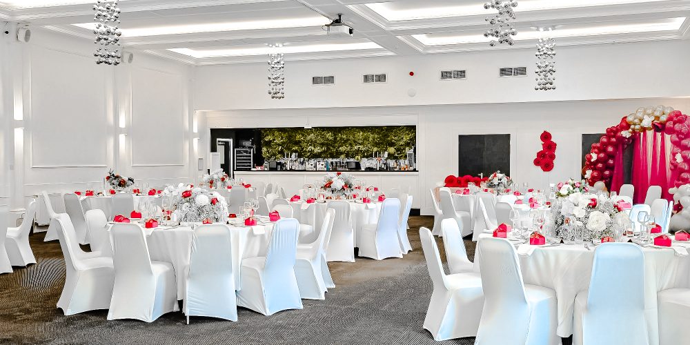 Wedding reception room at Woodbourne House with round tables, white chair covers and red accents.
