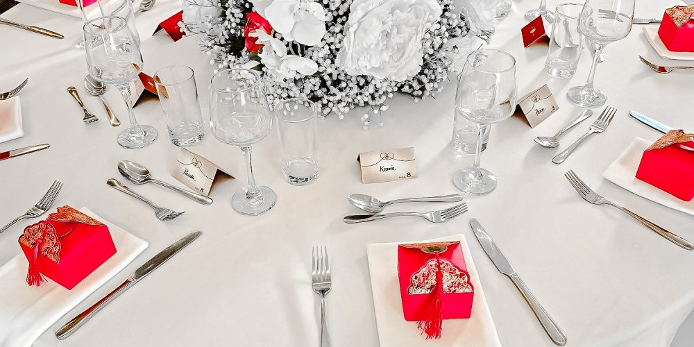 Wedding reception table at Woodbourne House with white floral centrepiece and red place settings.